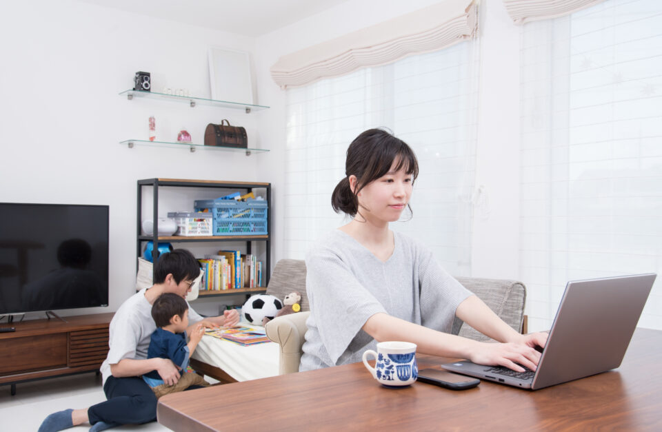 父親が子どもの相手をしているリビングで仕事をしている主婦