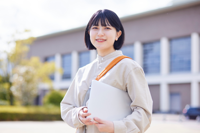 ノートパソコンを小脇に抱えてこちらを見ている笑顔の女性